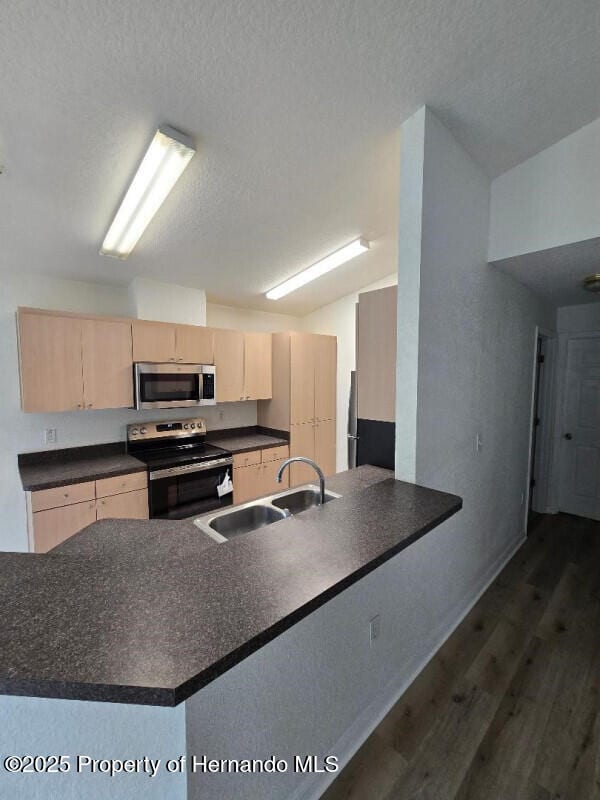 kitchen featuring appliances with stainless steel finishes, light brown cabinetry, a sink, dark countertops, and a textured ceiling