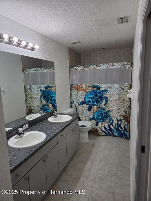 full bathroom featuring a textured ceiling, toilet, double vanity, and curtained shower