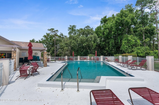 community pool featuring a patio, fence, and view of wooded area