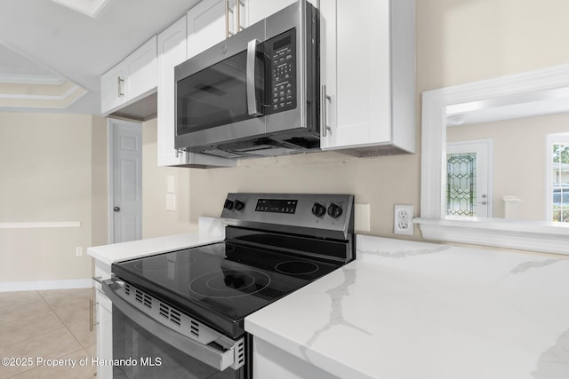 kitchen with stainless steel appliances, white cabinetry, light stone counters, and light tile patterned flooring