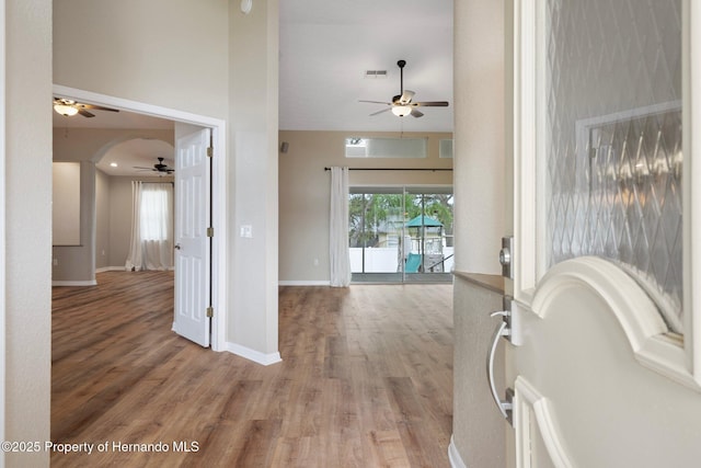 entryway featuring ceiling fan, light wood-style floors, baseboards, and a towering ceiling