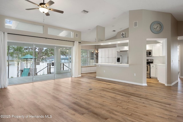 unfurnished living room with ceiling fan, light wood-style flooring, high vaulted ceiling, baseboards, and a chandelier