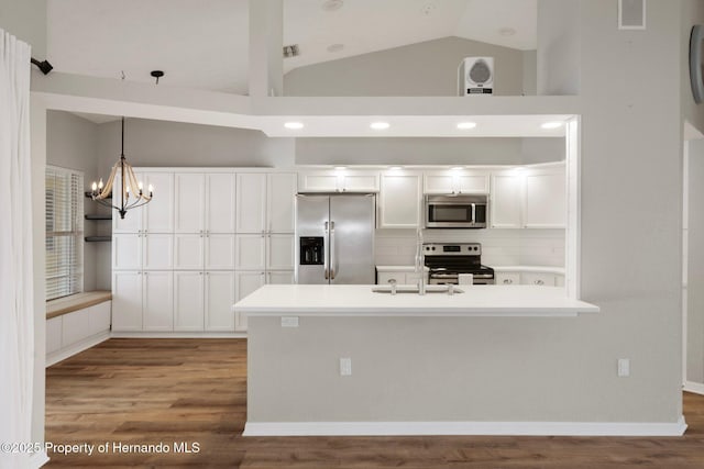 kitchen featuring appliances with stainless steel finishes, white cabinets, lofted ceiling, wood finished floors, and a sink