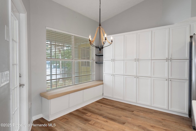 unfurnished dining area featuring a chandelier, light wood-style flooring, and lofted ceiling