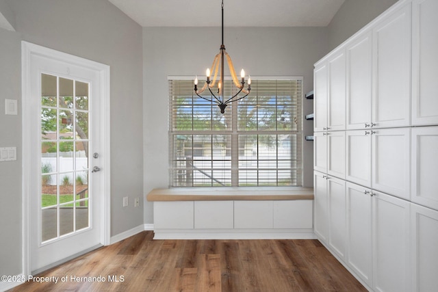 unfurnished dining area with a chandelier, dark wood-style flooring, and baseboards