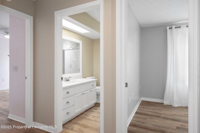 bathroom with wood finished floors, vanity, toilet, and baseboards