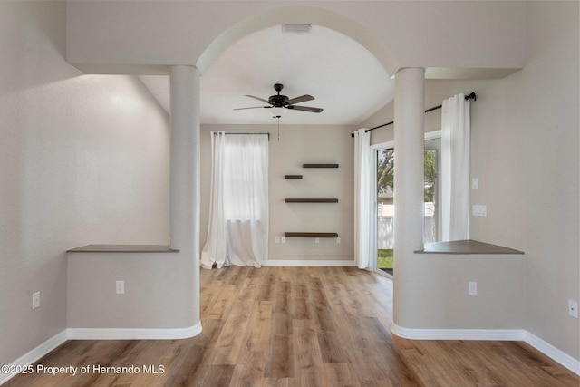spare room featuring decorative columns, a ceiling fan, wood finished floors, baseboards, and arched walkways