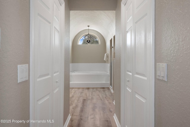 hall with a textured wall, a chandelier, and light wood-type flooring