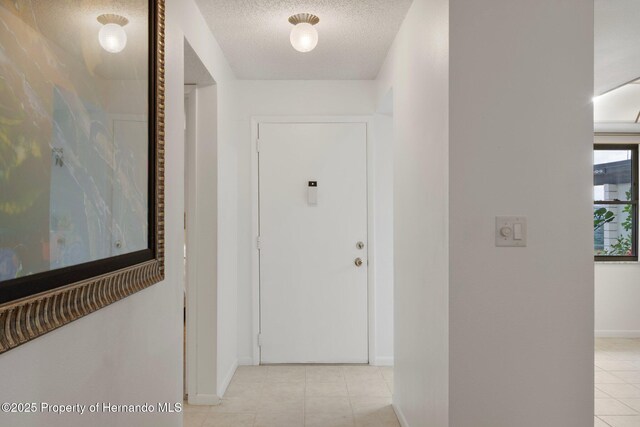 corridor featuring baseboards, a textured ceiling, and light tile patterned floors