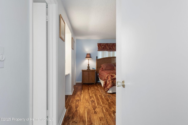 bedroom with wood finished floors, a textured ceiling, and baseboards