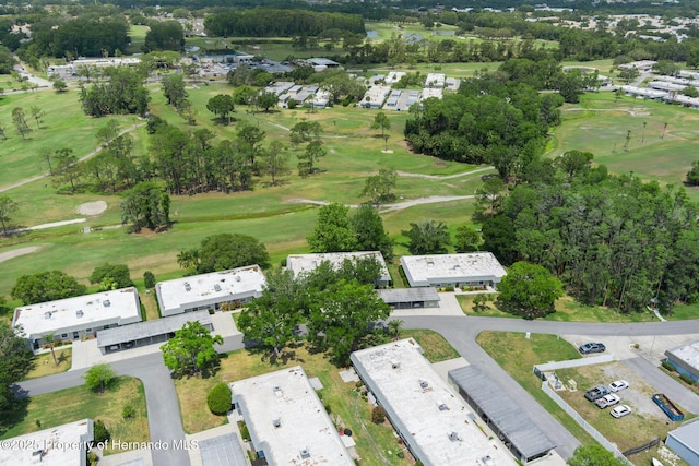 aerial view of property and surrounding area featuring a golf club and a tree filled landscape