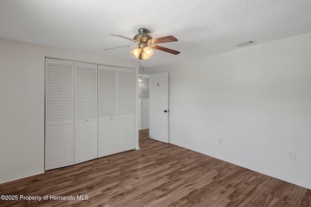 unfurnished bedroom with wood finished floors, a closet, a textured ceiling, ceiling fan, and baseboards