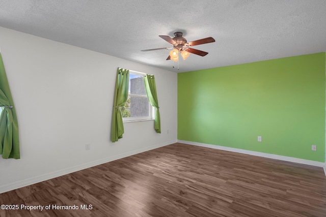 empty room with a textured ceiling, wood finished floors, a ceiling fan, and baseboards