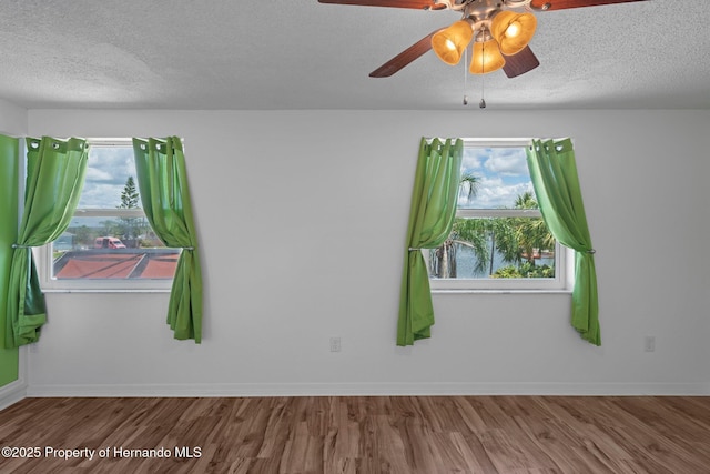 empty room with a textured ceiling, wood finished floors, a ceiling fan, and baseboards