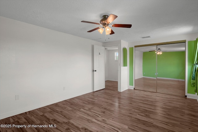 unfurnished bedroom featuring wood finished floors, baseboards, ceiling fan, a closet, and a textured ceiling