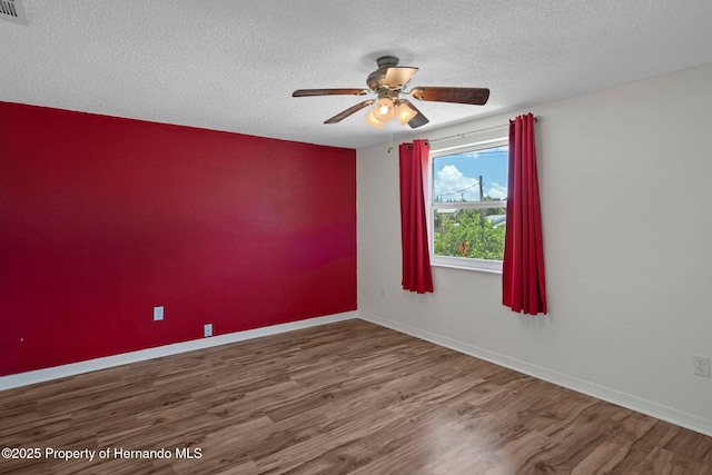 empty room with a textured ceiling, wood finished floors, a ceiling fan, and baseboards
