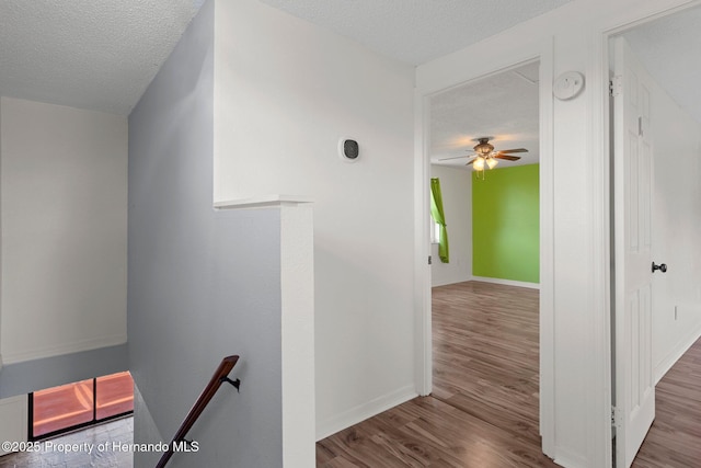 hallway featuring an upstairs landing, a textured ceiling, wood finished floors, and baseboards