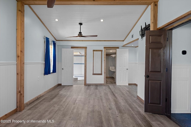 unfurnished living room featuring lofted ceiling, wainscoting, ceiling fan, wood finished floors, and ornamental molding