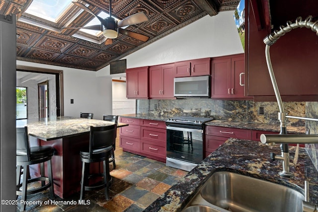 kitchen featuring stainless steel appliances, backsplash, dark brown cabinets, ceiling fan, and dark stone finish floors