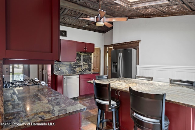 kitchen featuring stainless steel appliances, a ceiling fan, reddish brown cabinets, an ornate ceiling, and dark stone counters