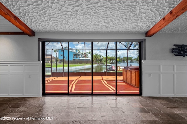 entryway featuring beamed ceiling, a decorative wall, stone tile floors, and wainscoting
