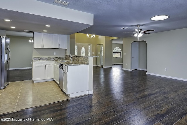 kitchen featuring stainless steel appliances, a sink, a peninsula, open floor plan, and dark stone countertops