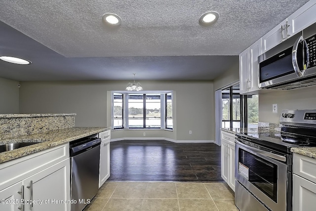 kitchen featuring stainless steel appliances, a chandelier, white cabinetry, light stone counters, and a textured ceiling