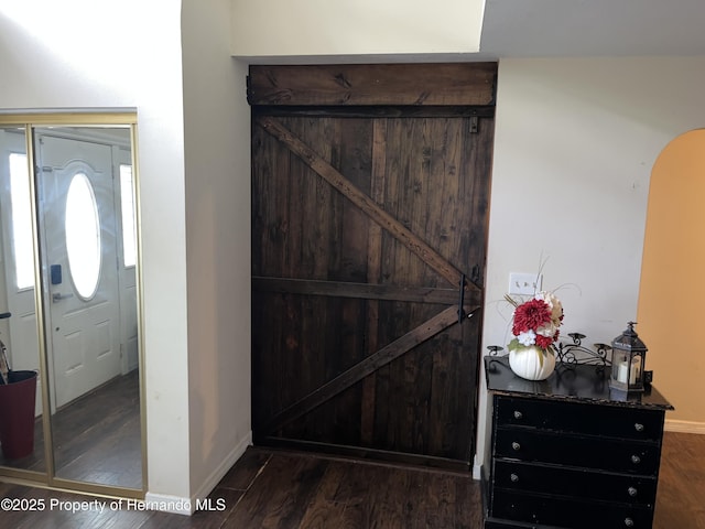 entryway with arched walkways, dark wood-style floors, and baseboards
