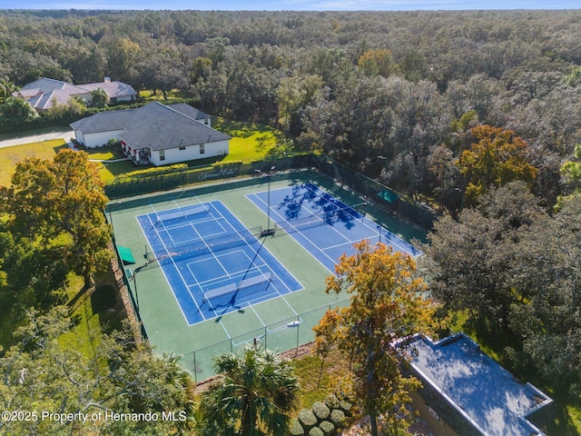 view of tennis court with a wooded view and fence