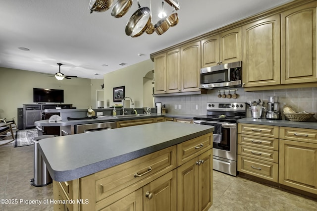 kitchen with appliances with stainless steel finishes, a sink, dark countertops, tasteful backsplash, and ceiling fan