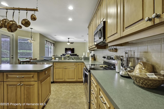 kitchen featuring appliances with stainless steel finishes, a peninsula, a sink, dark countertops, and a ceiling fan