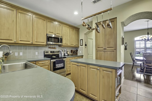 kitchen with appliances with stainless steel finishes, a sink, arched walkways, a chandelier, and tasteful backsplash