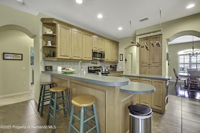 kitchen featuring appliances with stainless steel finishes, arched walkways, a peninsula, tasteful backsplash, and open shelves