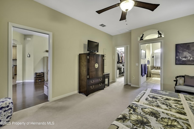 bedroom featuring a walk in closet, light colored carpet, ensuite bath, baseboards, and a closet