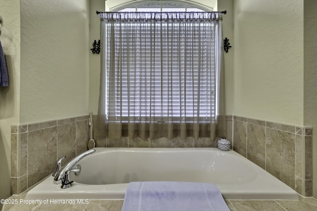 full bathroom featuring a garden tub, healthy amount of natural light, and a textured wall