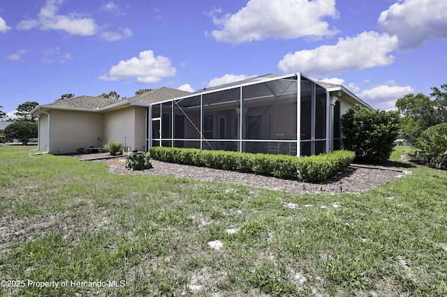back of house with a lawn, a lanai, and stucco siding