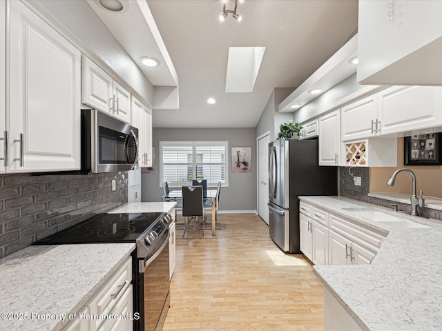 11350 Copley Ct, Spring Hill, FL 34609 - kitchen featuring appliances with stainless steel finishes, a sink, a skylight, light wood-style floors, and white cabinetry