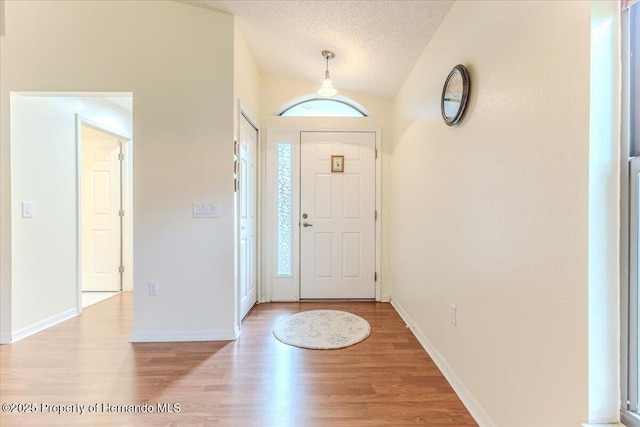 entrance foyer featuring light wood-style flooring, plenty of natural light, baseboards, lofted ceiling, and a textured ceiling
