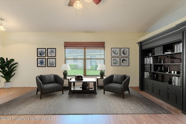 living area featuring wood finished floors, ceiling fan, and baseboards