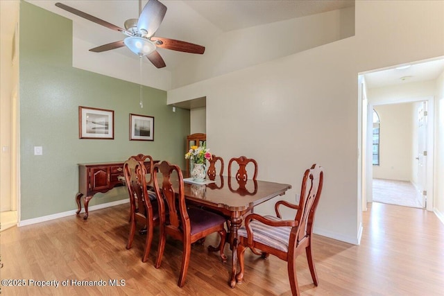 dining space with light wood finished floors, a ceiling fan, vaulted ceiling, and baseboards