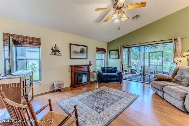 living area featuring lofted ceiling, ceiling fan, plenty of natural light, wood finished floors, and a glass covered fireplace