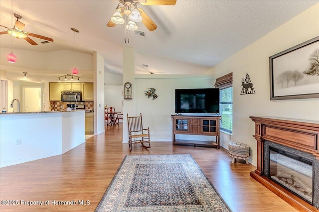living room featuring a ceiling fan, lofted ceiling, light wood-style flooring, and a glass covered fireplace