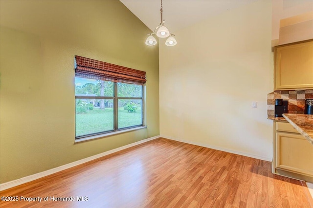 unfurnished dining area featuring light wood-type flooring, baseboards, and vaulted ceiling