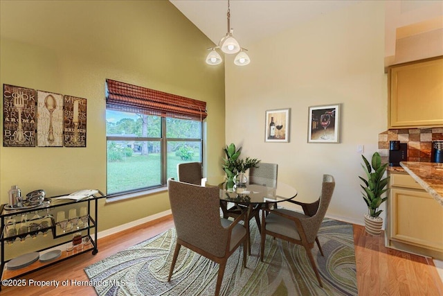dining space with light wood-style flooring, baseboards, and high vaulted ceiling