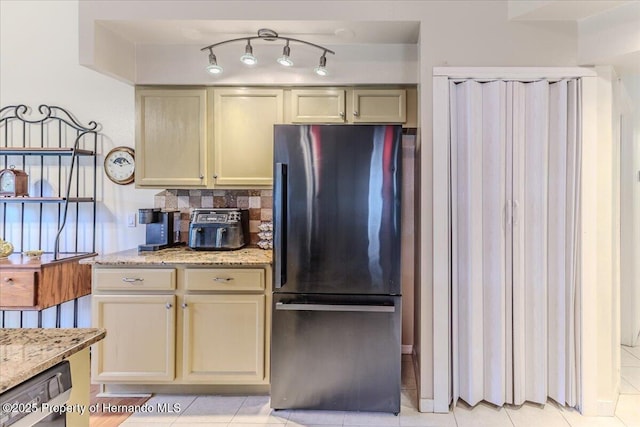 kitchen with freestanding refrigerator, light stone counters, backsplash, light tile patterned floors, and cream cabinetry