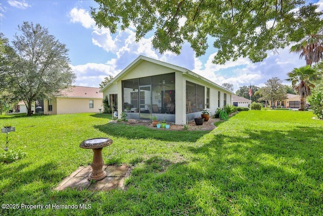 back of property with a yard, a sunroom, and stucco siding