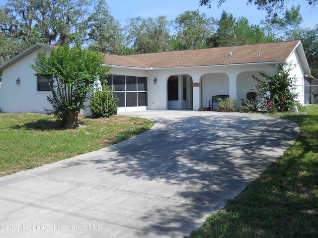 ranch-style home with stucco siding, driveway, and a front lawn