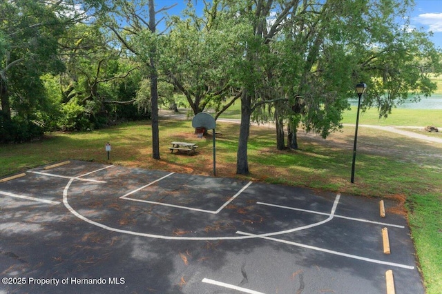view of basketball court with basketball hoop and a lawn