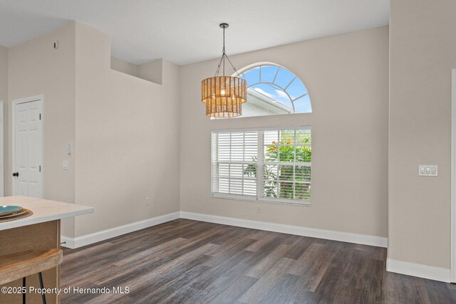 unfurnished dining area with a chandelier, dark wood-style floors, and baseboards