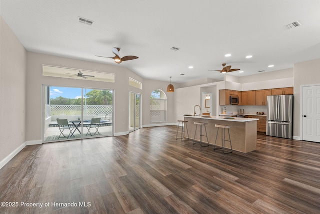 kitchen with appliances with stainless steel finishes, brown cabinets, open floor plan, dark wood finished floors, and a sink